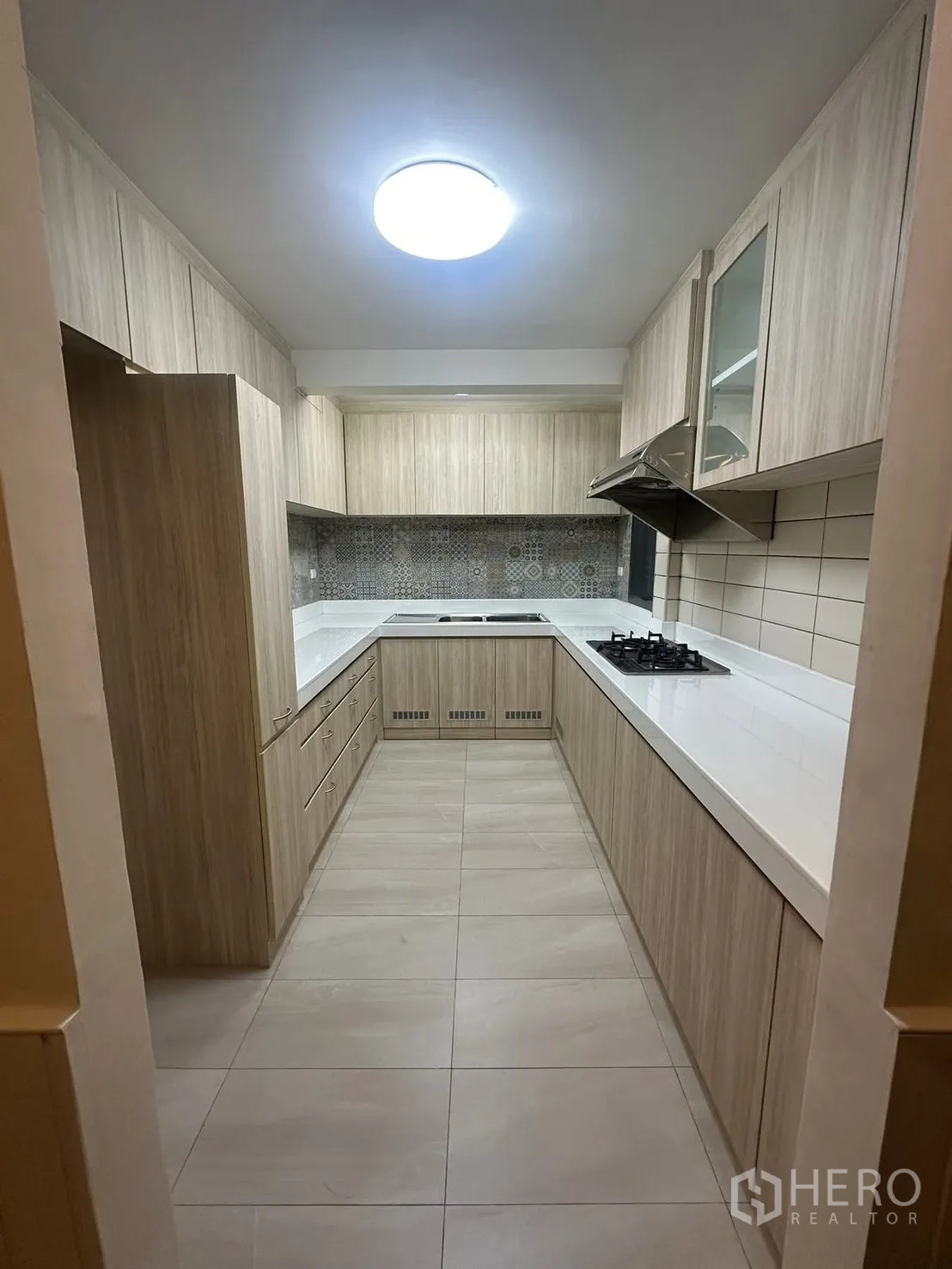 Detached House for rent in Watthana, Bangkok - U-shaped kitchen with light wood cabinetry, gas cooktop, range hood and ample storage.