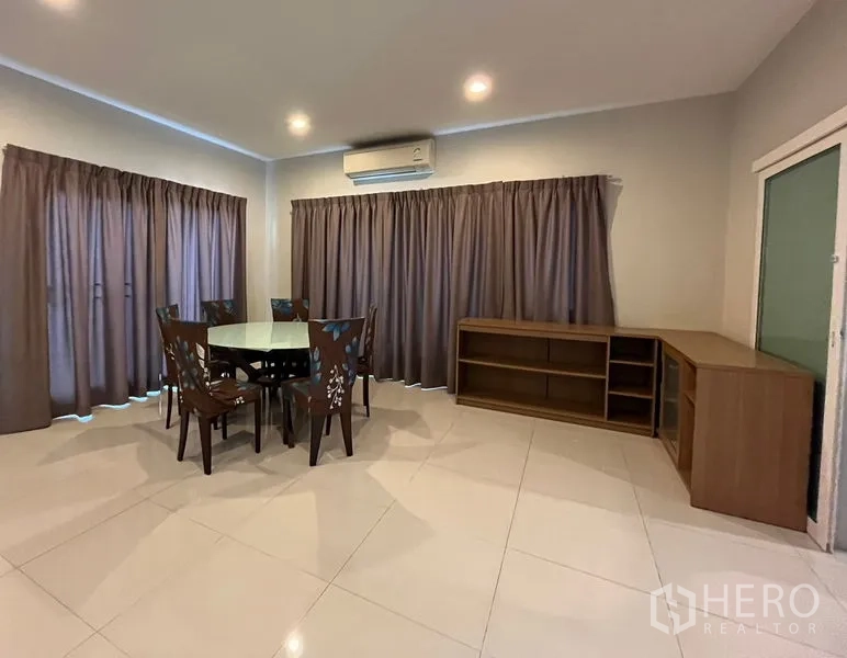 Detached House for rent or sale in Bang Na, Bangkok - Dining room with round glass table, air conditioning and full-length curtains.