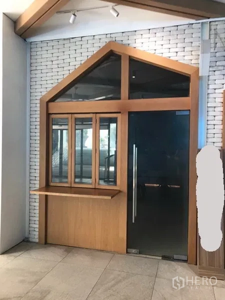 Retail Space for rent in Watthana, Bangkok - Compact retail unit with wood-framed glass storefront, counter window and black glass door against a white brick wall.