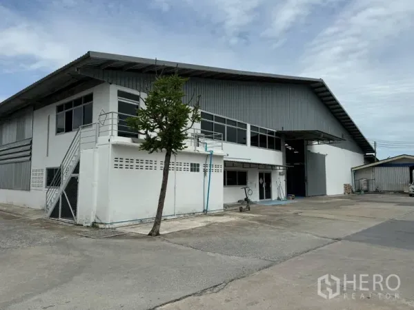 Warehouse for rent in Mueang Pathum Thani, Pathum Thani - Angled exterior of the warehouse showing long windows, metal roof, and broad internal driveway.