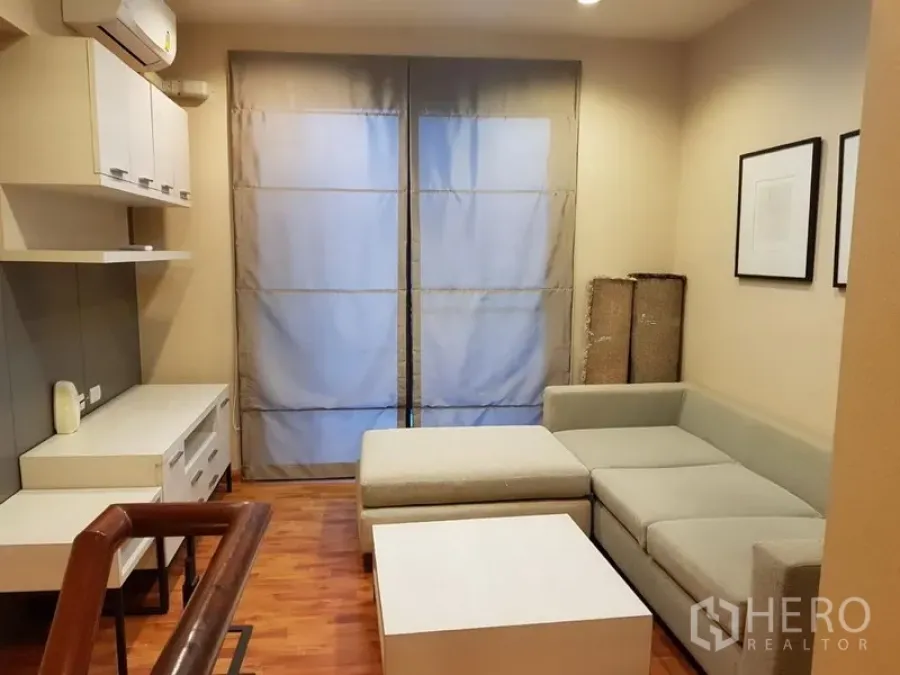 Townhouse for rent in Phra Khanong, Bangkok - Cozy upstairs living room with L-shaped sofa, coffee table and large curtained windows on wood flooring.