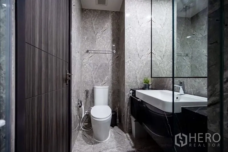 Condominium for rent in Watthana, Bangkok - Bathroom with toilet, large mirror and marble tiling.