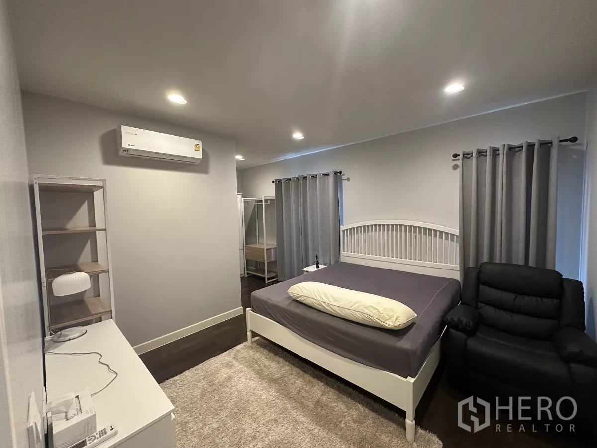 Detached House for rent or sale in Lam Luk Ka, Pathum Thani - Master bedroom with bed, recliner, rug, grey curtains and air conditioning for comfort.