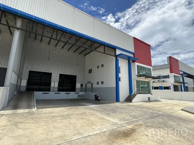 Factory for rent in Mueang Samut Prakan, Samut Prakan - Covered loading dock with ramp access, wide roller shutters, and ample truck turning space.