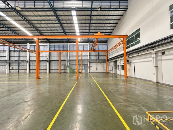 Factory for sale in Lam Luk Ka, Pathum Thani - Spacious factory hall with orange overhead crane, epoxy flooring, and safety lines.