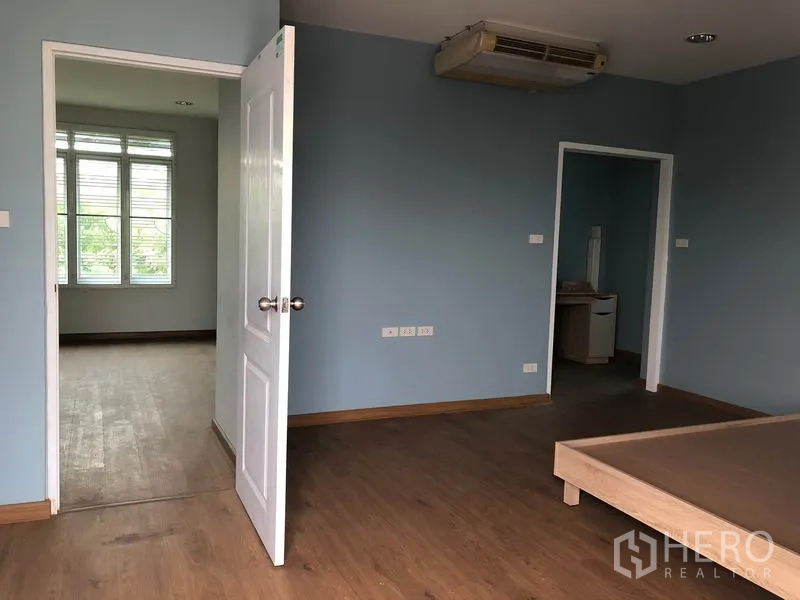 Detached House for sale in Bang Khen, Bangkok - Master bedroom angle showing large windows, doorway to adjoining room and wood floors.