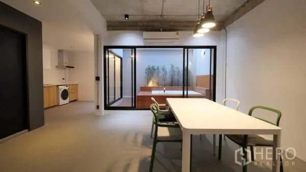 Townhouse for rent in Khlong Toei, Bangkok - Dining area with pendant lights facing sliding glass doors to a courtyard with a built-in jacuzzi.