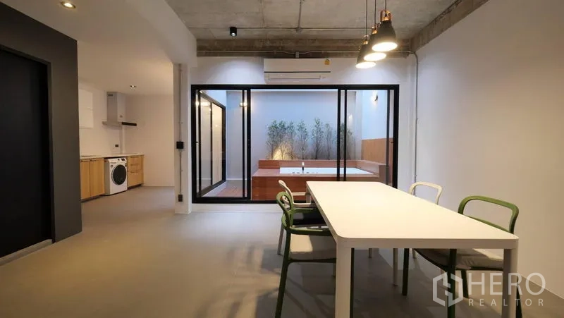 Townhouse for rent in Khlong Toei, Bangkok - Dining area with pendant lights facing sliding glass doors to a courtyard with a built-in jacuzzi.