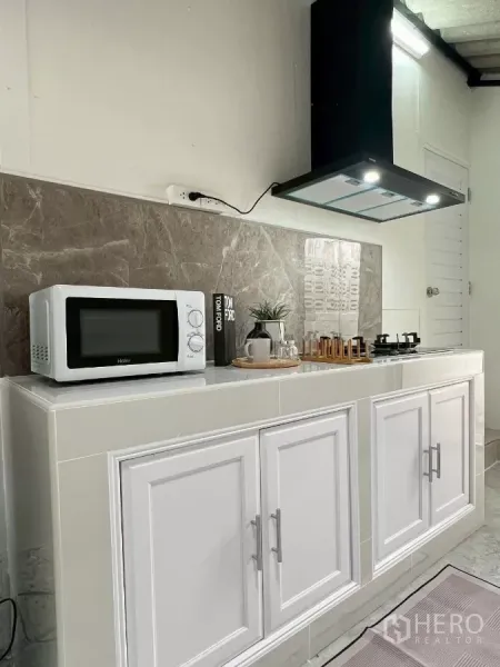 Detached House for rent in Huai Khwang, Bangkok - Compact kitchen with white cabinets, microwave, marble backsplash and a range hood.