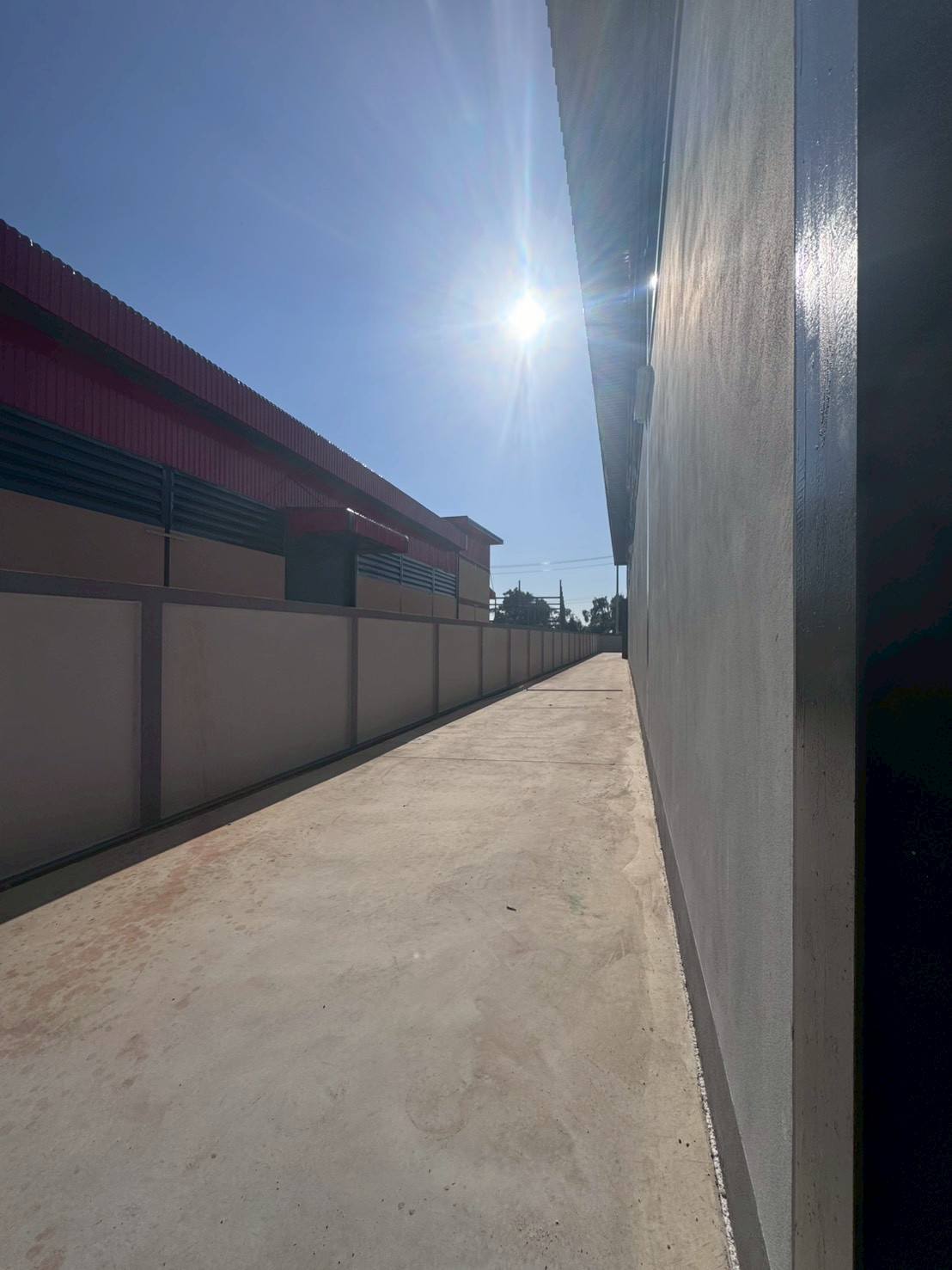Factory for sale in Mueang Samut Sakhon, Samut Sakhon - Side driveway along the building with boundary wall and afternoon sunlight.