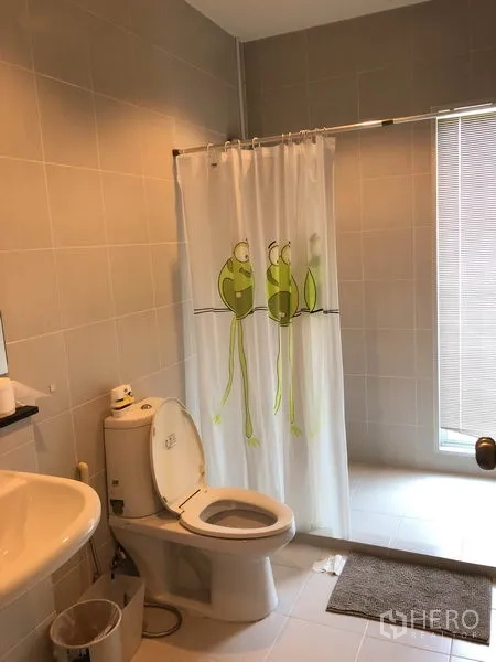 Townhouse for rent or sale in Suan Luang, Bangkok - Second bathroom finished in beige tiles with shower area behind curtain, toilet and basin.