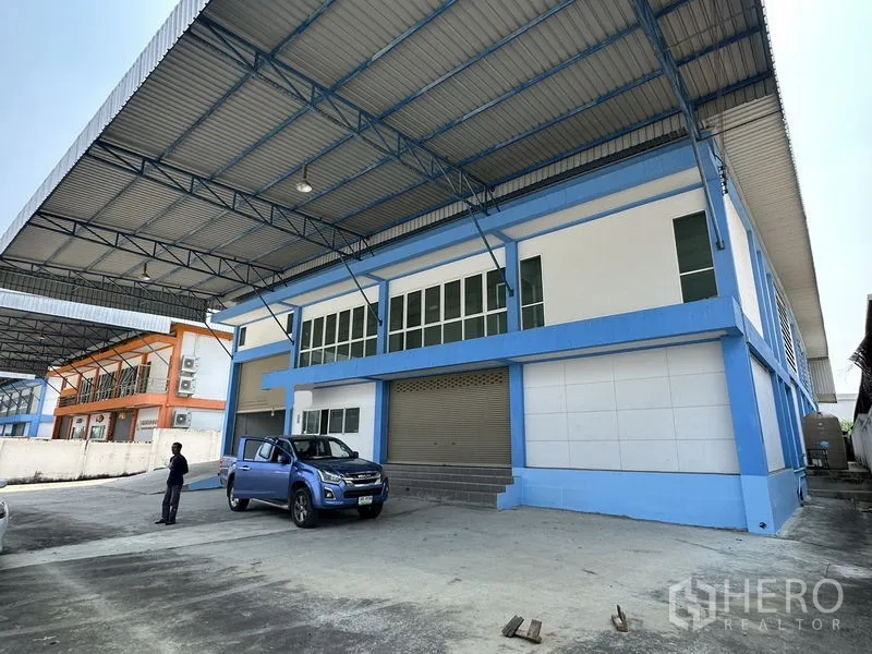 工厂 出租在Bang Bo, Samut Prakan - 工厂正立面，带遮雨装卸区、玻璃办公室窗与大卷帘门。