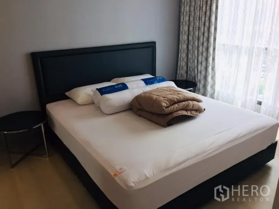 Condominium for rent in Khlong Toei, Bangkok - Master bedroom with upholstered bed, bedside tables and tall window with curtains.