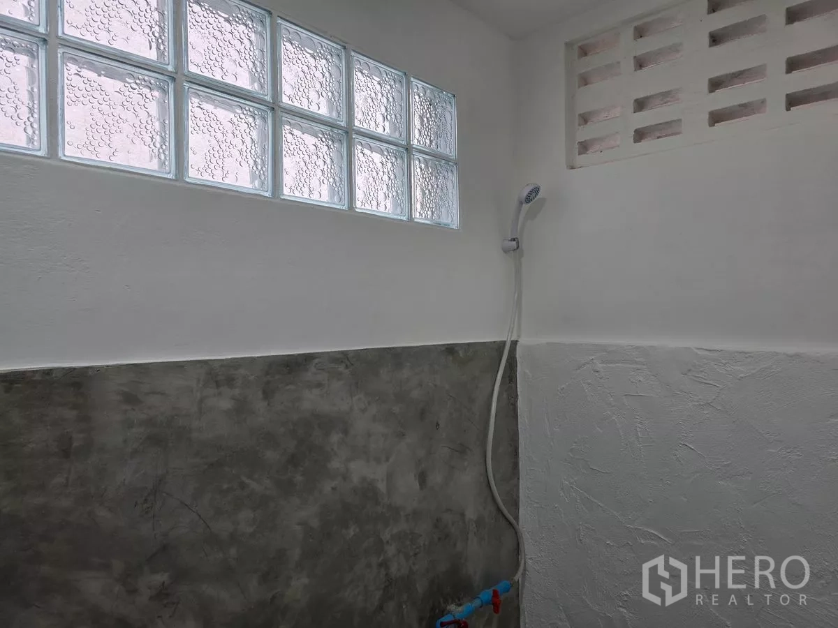 Shophouse for rent in Watthana, Bangkok - Minimalist bathroom with handheld shower and glass‑block window allowing natural light.