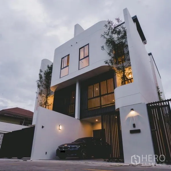 Townhouse for sale in Phra Khanong, Bangkok - Gated contemporary townhouse exterior with a car parked in the covered driveway at twilight.