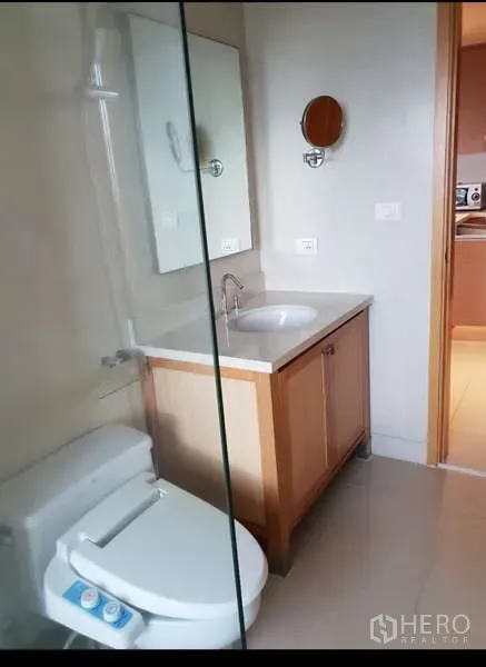 Condominium for rent - Modern bathroom with glass shower screen, vanity and bidet toilet, with kitchen visible through the doorway.