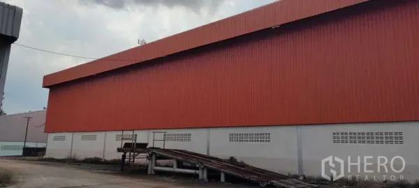 Warehouse for rent in Nikhom Phatthana, Rayong - Side exterior of an orange metal-clad warehouse with loading ramp and service yard in Nikhom Phatthana, Rayong.