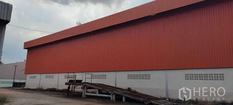 Warehouse for rent in Nikhom Phatthana, Rayong - Side exterior of an orange metal-clad warehouse with loading ramp and service yard in Nikhom Phatthana, Rayong.