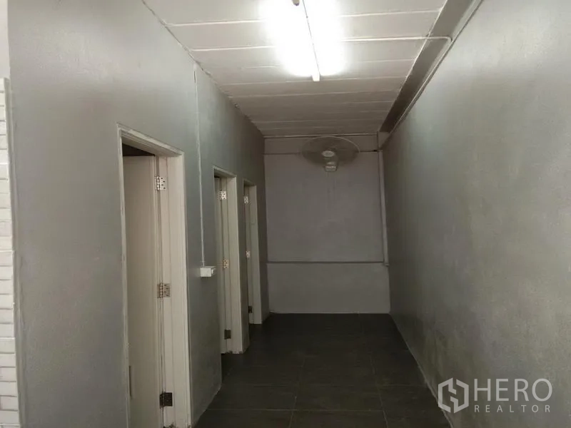 Warehouse for rent in Bang Phli, Samut Prakan - Corridor leading to staff restrooms and utility rooms with gray walls and ceiling lighting.