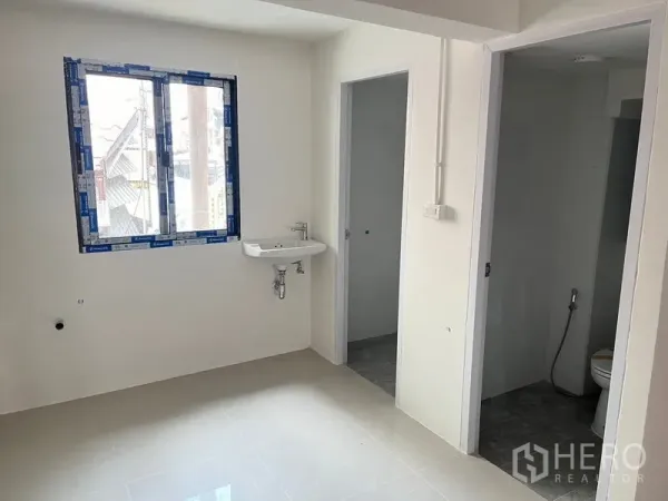 Retail Space for rent - Back room featuring a window, wall‑mounted sink, and two doorways for storage and WC.