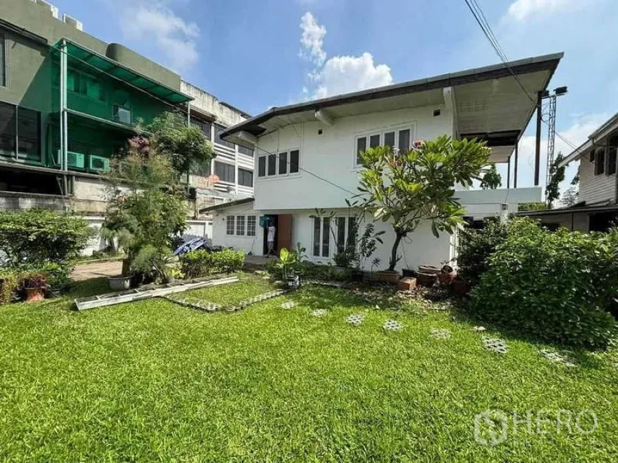 独立式住宅 出租在Suan Luang, Bangkok - 白色两层房屋面向阳光草坪和灌木花园，庭院空间宽敞。