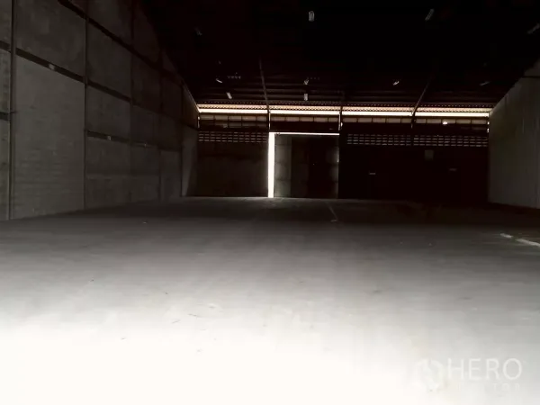Warehouse for rent in Bang Phli, Samut Prakan - Spacious empty warehouse interior with high steel roof, concrete floor and a sliding door letting in light.