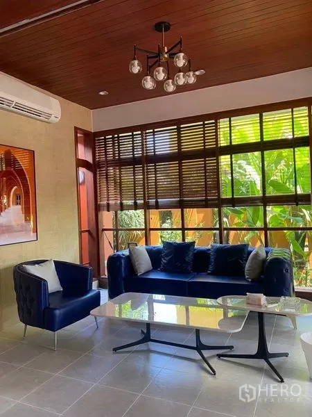 Detached House for rent in Suan Luang, Bangkok - Bright living room with blue sofa set, wooden ceiling and large windows facing the garden.
