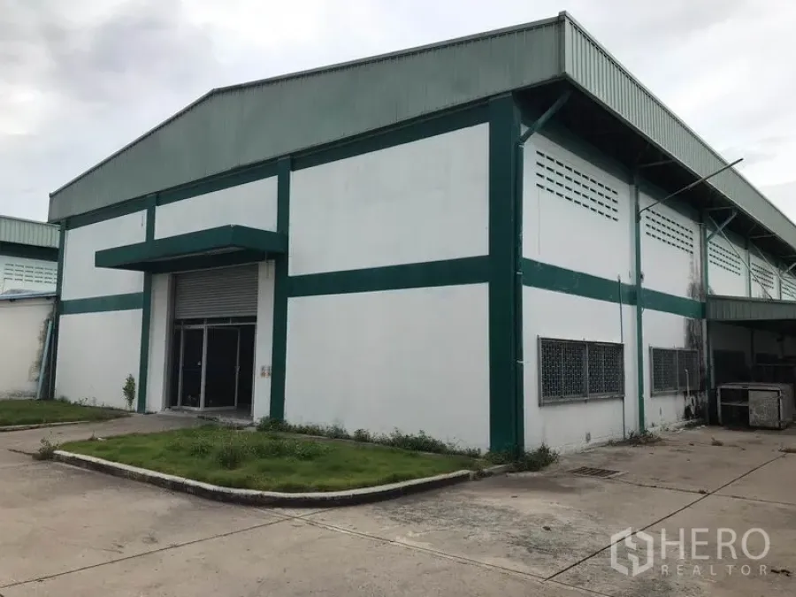 工厂 出租在Mueang Chon Buri, Chon Buri - 绿白色工厂外观，设卷闸门与混凝土车道，位于工业园区内