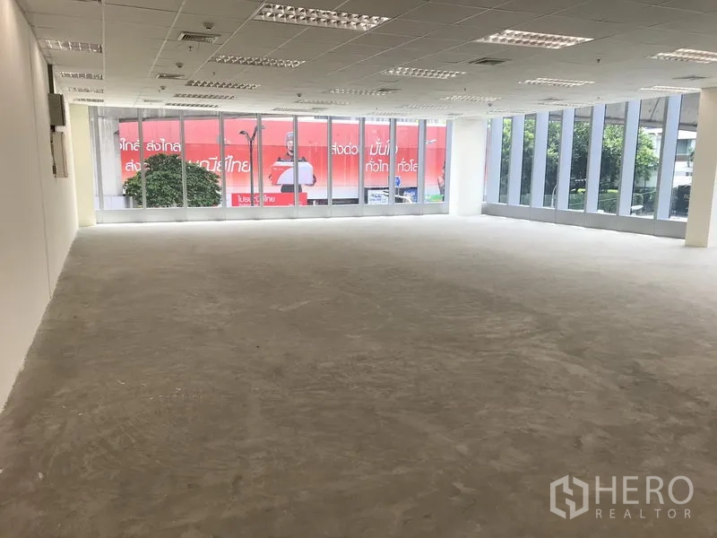 Office Space for rent in Khlong Toei, Bangkok - Open-plan office with floor-to-ceiling glass on two sides, grid ceiling lights, and an unfinished concrete floor.