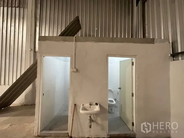 Warehouse for rent in Khlong Luang, Pathum Thani - Interior restroom block with two toilet rooms and a wall-mounted sink inside the warehouse.