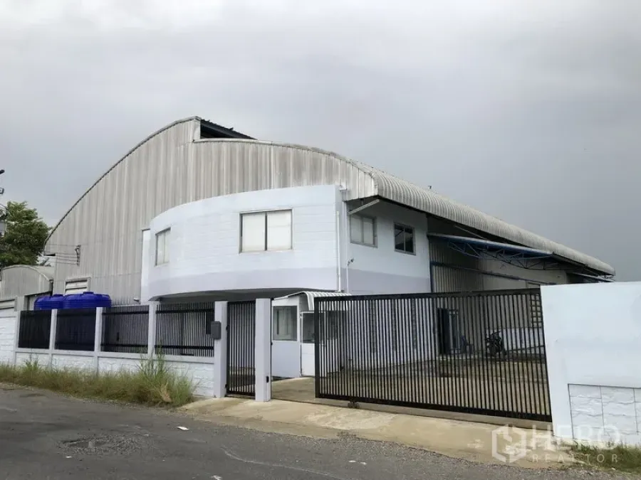 Factory for sale in Pathum Thani - Street-facing standalone warehouse with curved roof and two‑storey office behind a black gate.