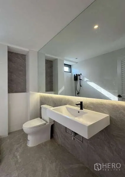 Townhouse for rent or sale in Prawet, Bangkok - Bathroom with long mirror, wall-hung sink, and shower niche.