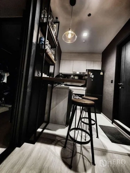 Condominium for sale in Pathum Wan, Bangkok - Open kitchen with breakfast bar, pendant light, and black fridge in a modern condo.