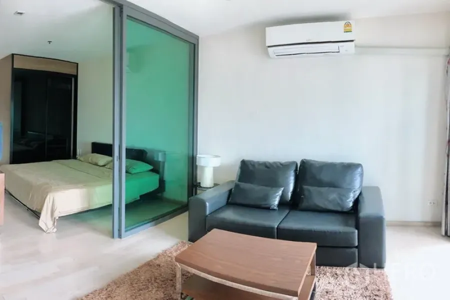 Condominium for rent in Khlong Toei, Bangkok - Noble Remix condo living area with leather sofa, coffee table and sliding glass wall to the bedroom under wall-mounted air conditioner.