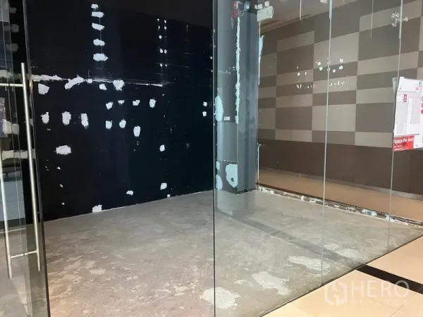 Retail Space for rent in Watthana, Bangkok - View through clear glass walls into a compact retail space with a black accent wall and polished mall tiles outside.