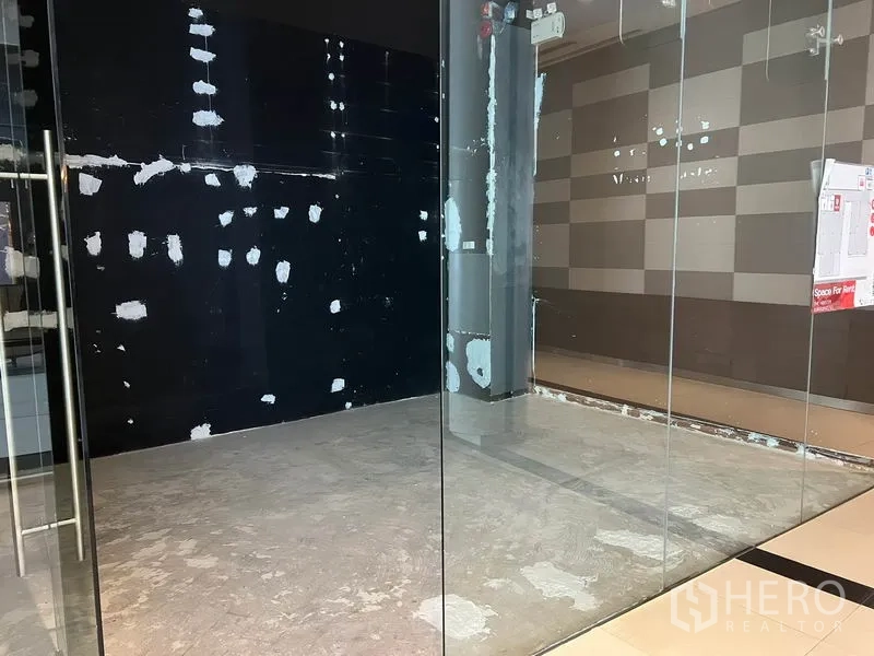 Retail Space for rent in Watthana, Bangkok - View through clear glass walls into a compact retail space with a black accent wall and polished mall tiles outside.
