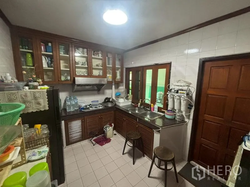 Detached House for sale in Suan Luang, Bangkok - Practical kitchen with tiled walls, upper glass cabinets and sink.