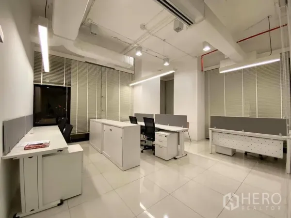 Office Space for rent in Bangkok - Open-plan office area with white desks, rolling chairs, high ceilings, blinds and LED strip lighting on glossy tile floors.