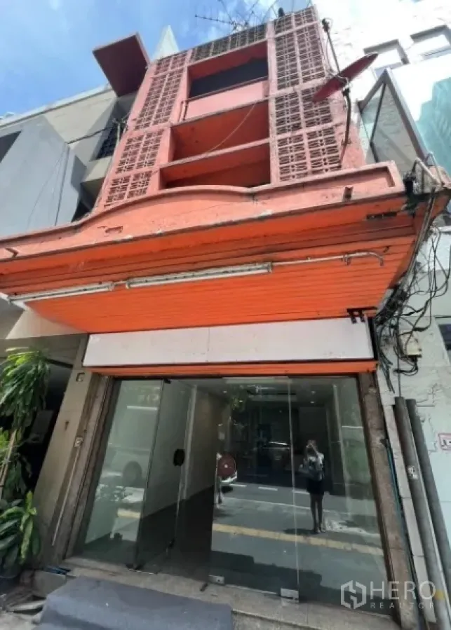 Shophouse for rent in Khlong Toei, Bangkok - Street-facing three-storey shophouse facade with orange metal shutter and glass storefront.