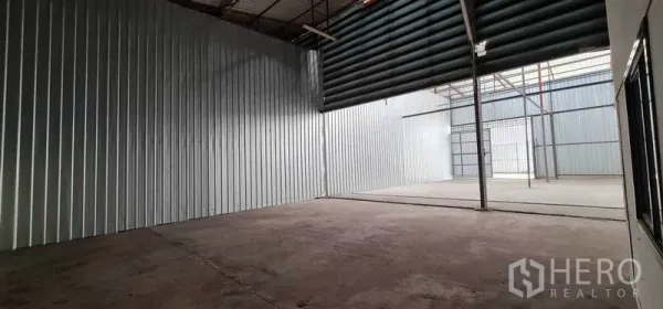 Warehouse for rent in Pak Kret, Nonthaburi - Open‑plan storage bay with a roller shutter and translucent roof panels for natural light.