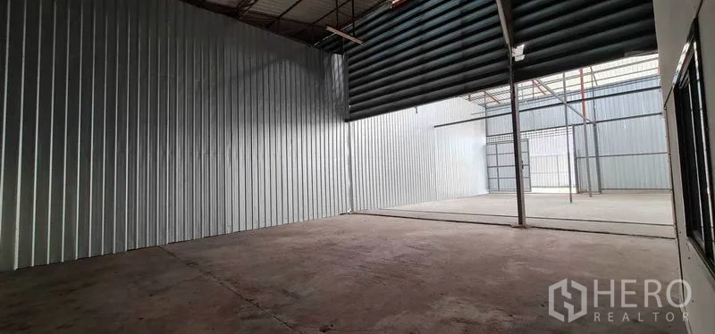 Warehouse for rent in Pak Kret, Nonthaburi - Open‑plan storage bay with a roller shutter and translucent roof panels for natural light.