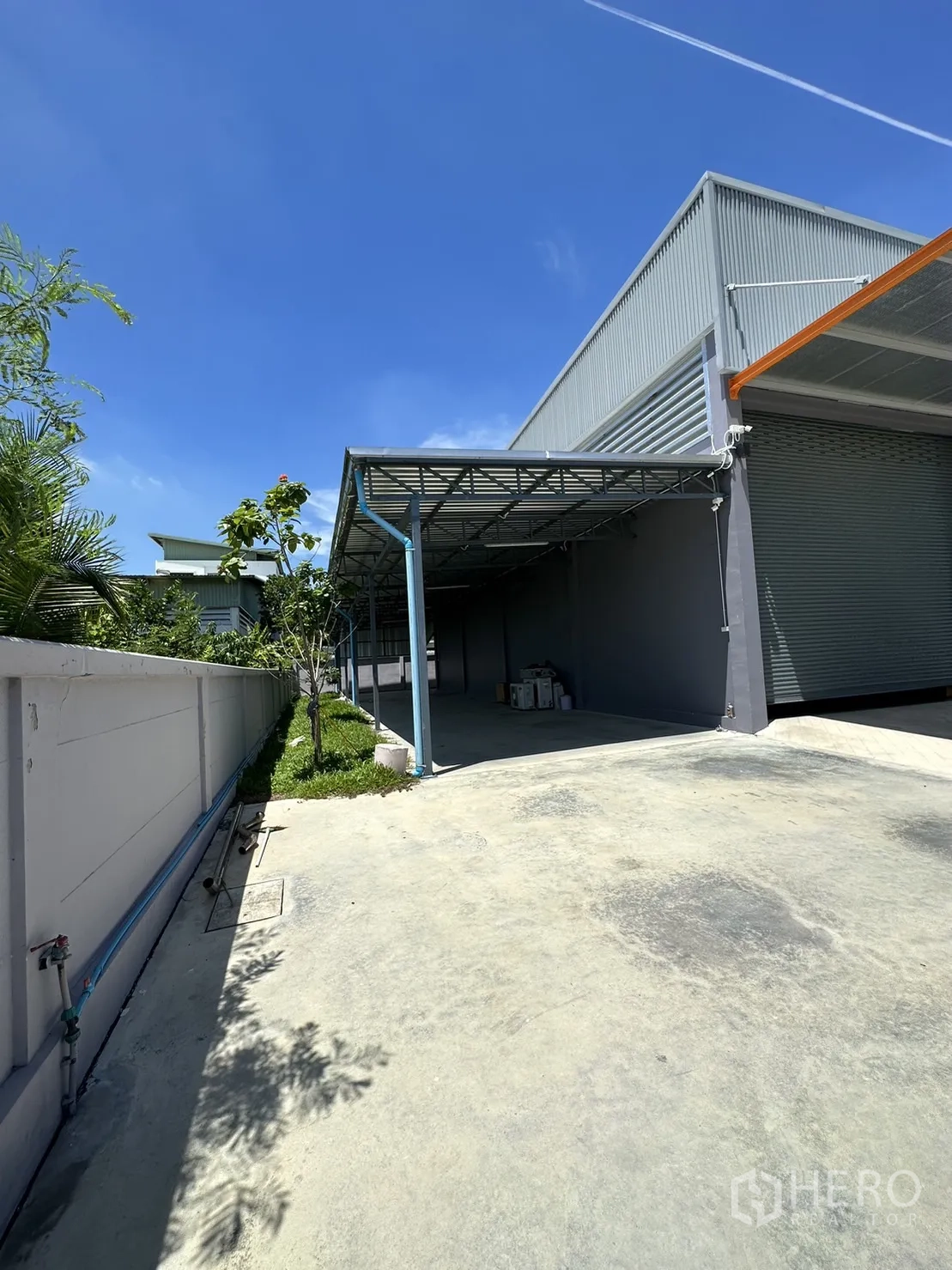 Factory for sale in Lam Luk Ka, Pathum Thani - Side yard with covered workspace and greenery along the wall.