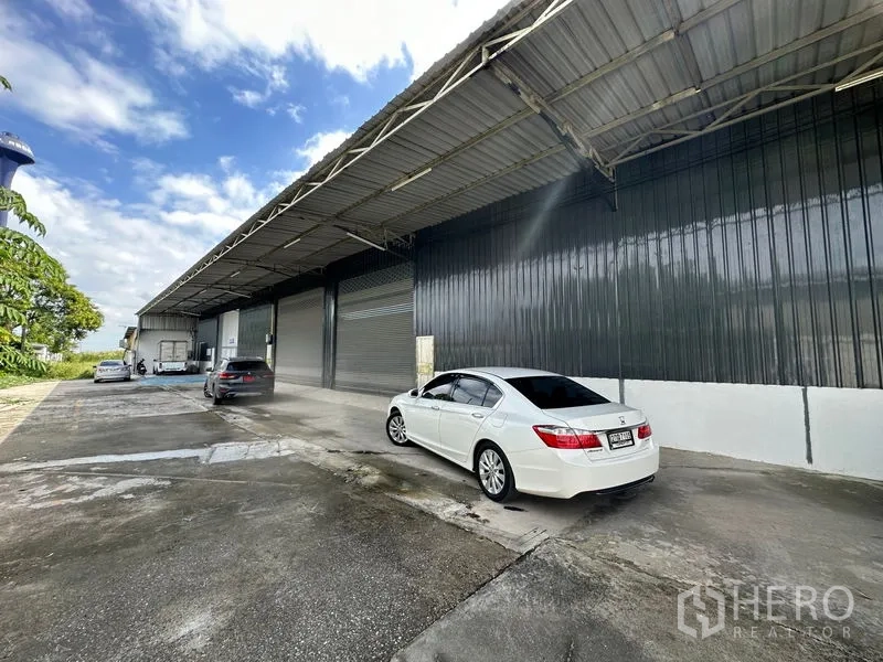 Warehouse for rent in Khlong Luang, Pathum Thani - Exterior facade with long canopy, parking area, and roll-up doors for easy truck access.
