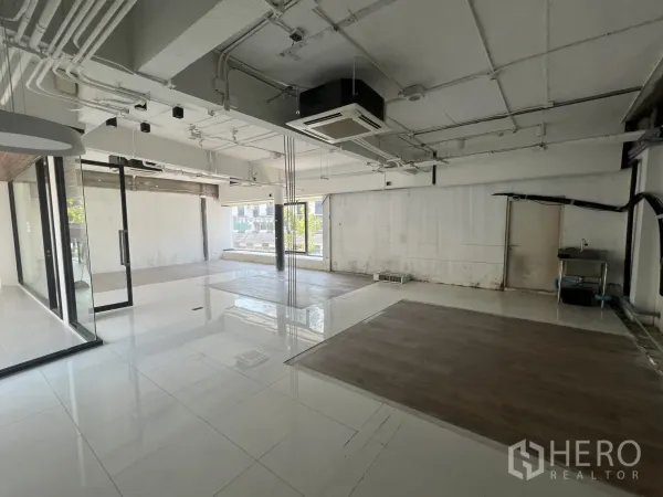 Retail Space for rent - Open-plan interior with white tile floors, exposed ceiling ducts and large windows.