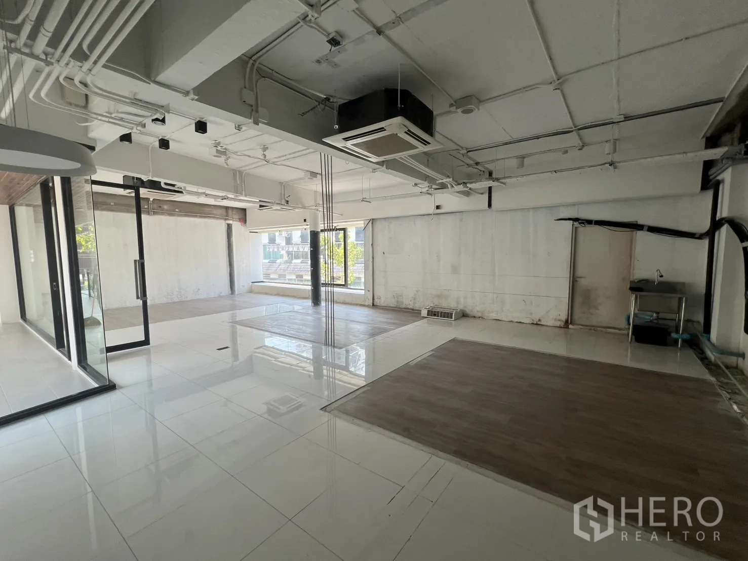 Retail Space for rent - Open-plan interior with white tile floors, exposed ceiling ducts and large windows.