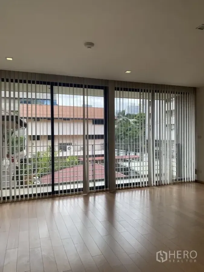 Condominium for rent in Pathum Wan, Bangkok - Bright condo living area with floor-to-ceiling windows, vertical blinds, and light wood floors overlooking the Pathum Wan neighborhood.
