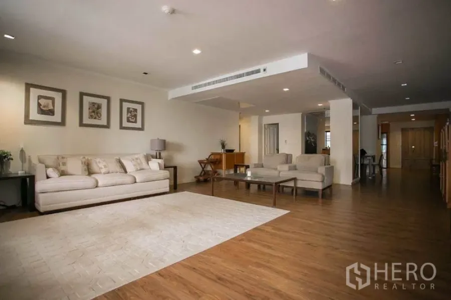 Condominium for rent or sale in Watthana, Bangkok - Spacious open-plan living room with wood flooring, cream sofa and recessed lighting.