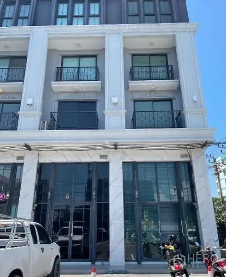 带办公室的家 出租或出售在Suan Luang, Bangkok - 4.5层商住办公楼外立面，挑高玻璃门面与上层阳台，前方设有停车区域。