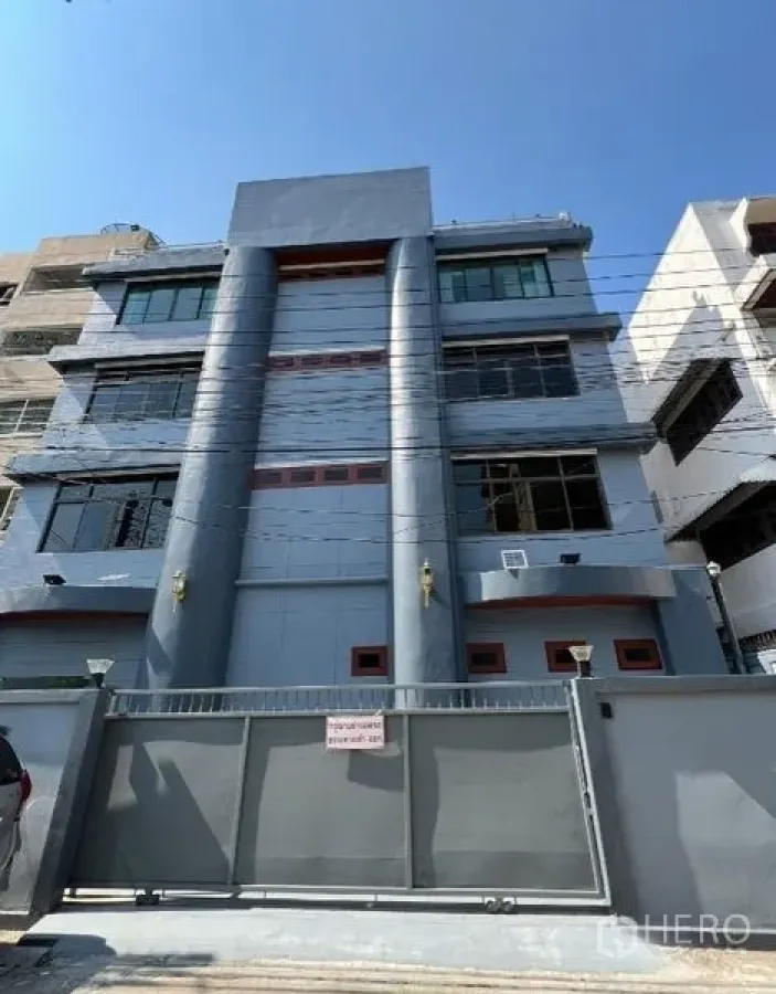Office Space for rent or sale in Khlong Toei, Bangkok - Four-storey gated office building in Bangkok with gray columns and wide windows under a blue sky.