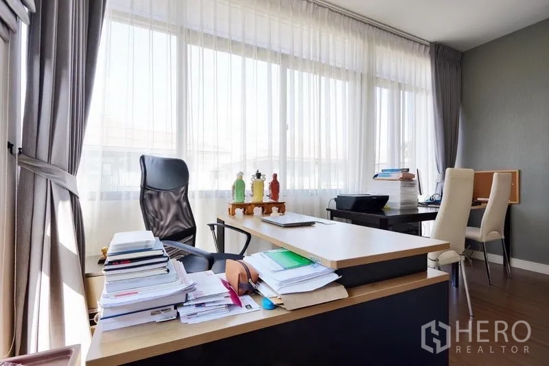 Detached House for rent or sale in Bang Kapi, Bangkok - Corner home office with L-shaped desk, executive chair and long sheer curtains along wide windows.